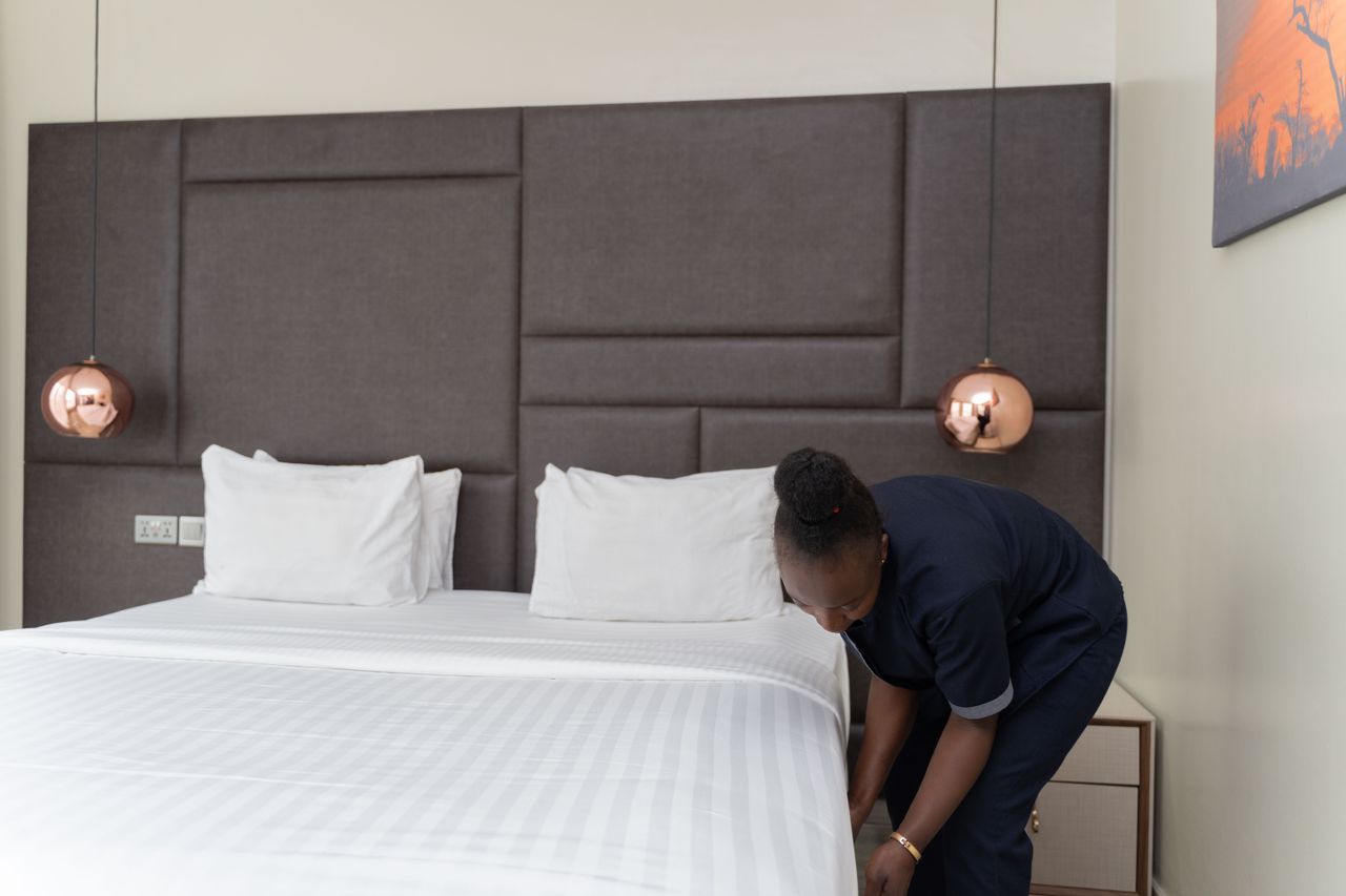 services-01 A hotel staff member prepares a bed in a sleek, modern hotel room with copper accents.