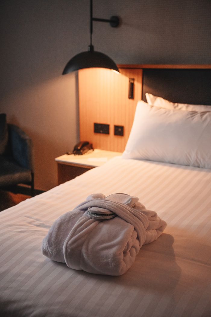 ours-journey A cozy hotel room featuring a plush robe on the bed under warm lighting, epitomizing comfort and relaxation.