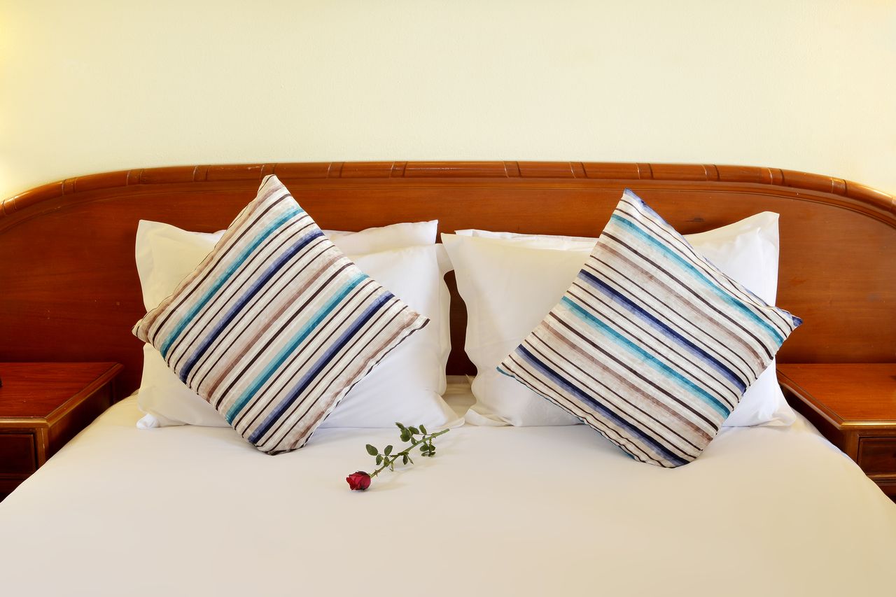 services-04 Elegant hotel bed setting with striped pillows and a red rose for a touch of romance.