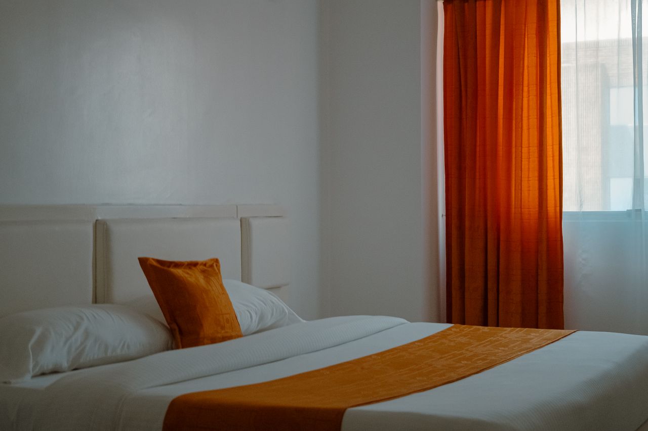 our-experience Warm and inviting hotel room with orange curtains and bedding creating a cozy ambiance.